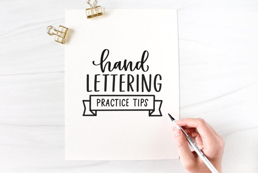 overhead view of a paper that says "hand lettering practice tips" with a hand holding a pen